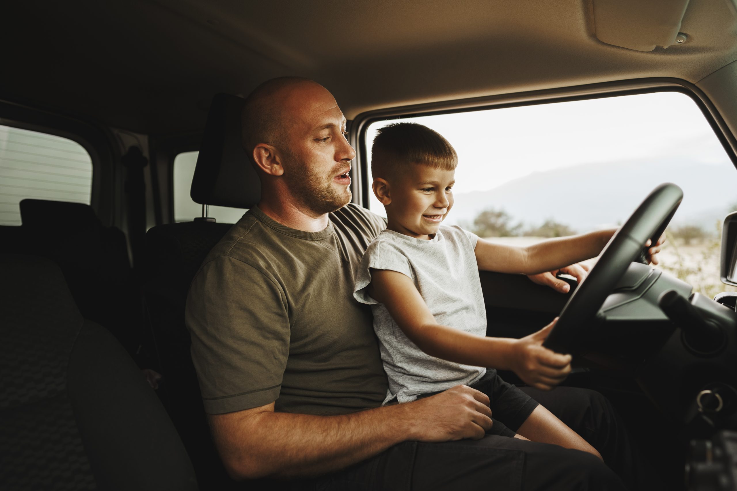 Father teaches little son to drive on road trip